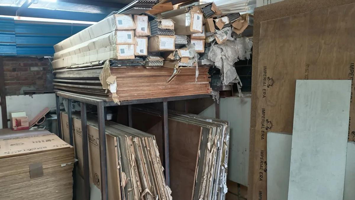 Warehouse racks of boards and laminate stock, with plywood sheets stacked alongside
