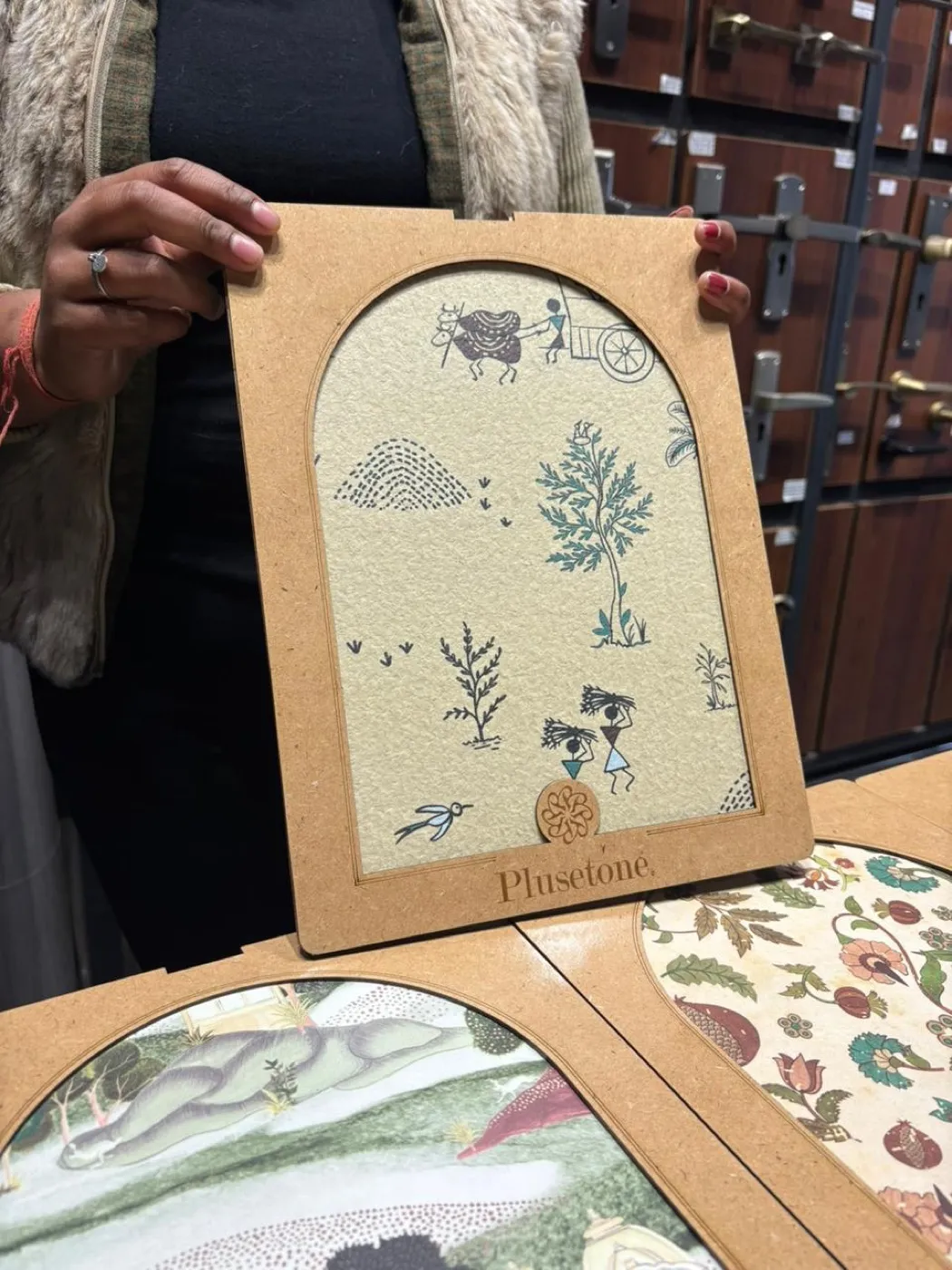 A Warli-style printed laminate sample held up in an arched frame in a showroom