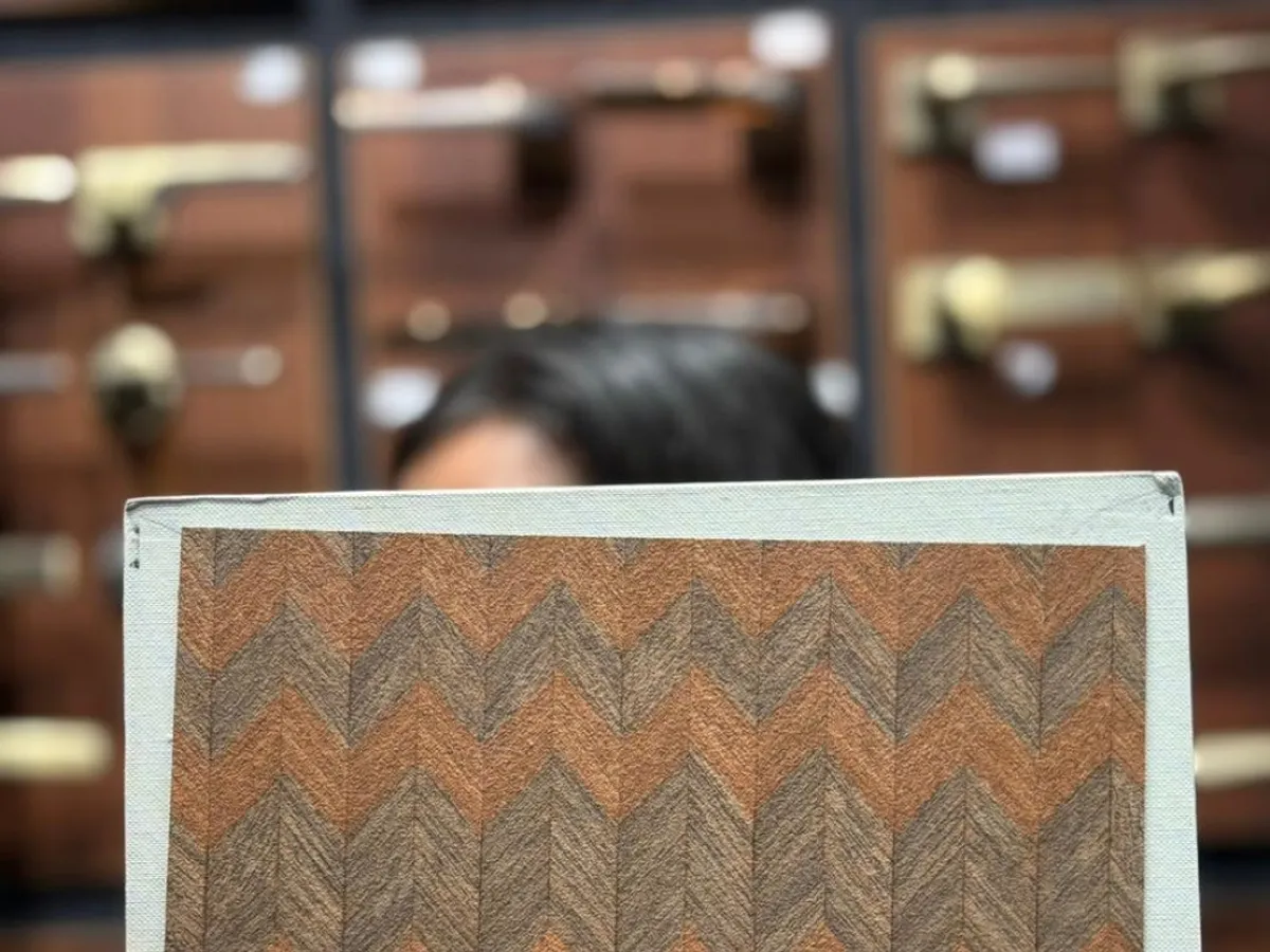 A hand holding a textured herringbone wood-pattern laminate sample